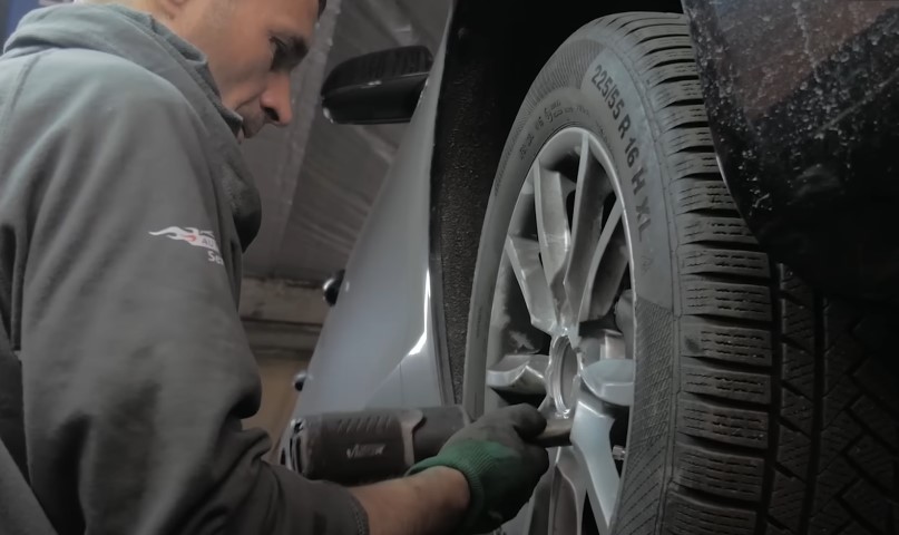 A mechanic uses a power tool to tighten the lug nuts on a car wheel
